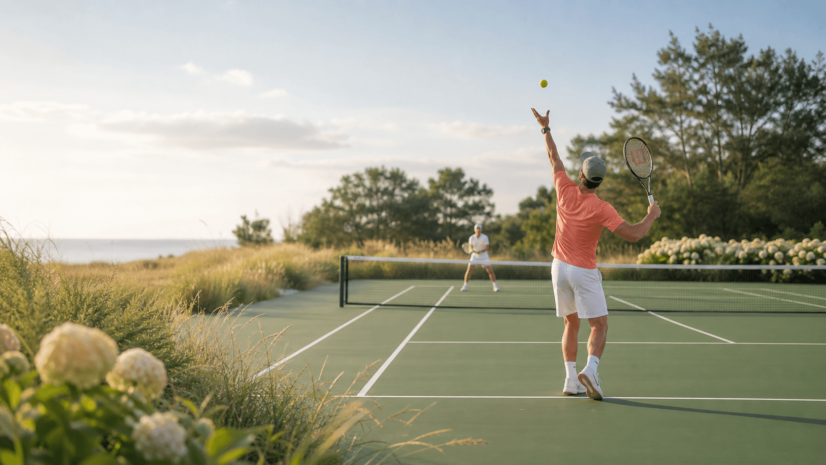 Tennis players on a coastal court bordered by dune grass and hydrangeas